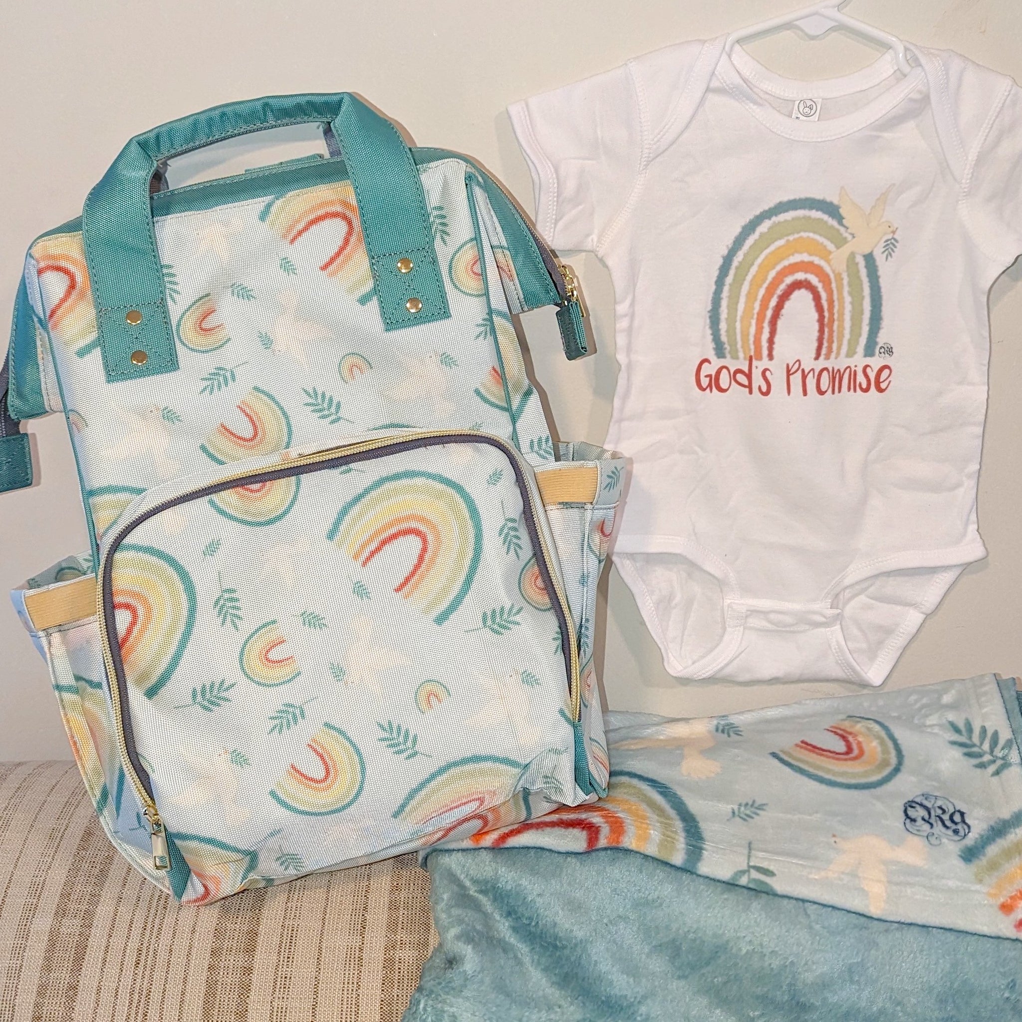 Catholic diaper bag, blanket, and bodysuit featuring God's Promise design based on Noah's Ark with rainbows, doves, and olive branches