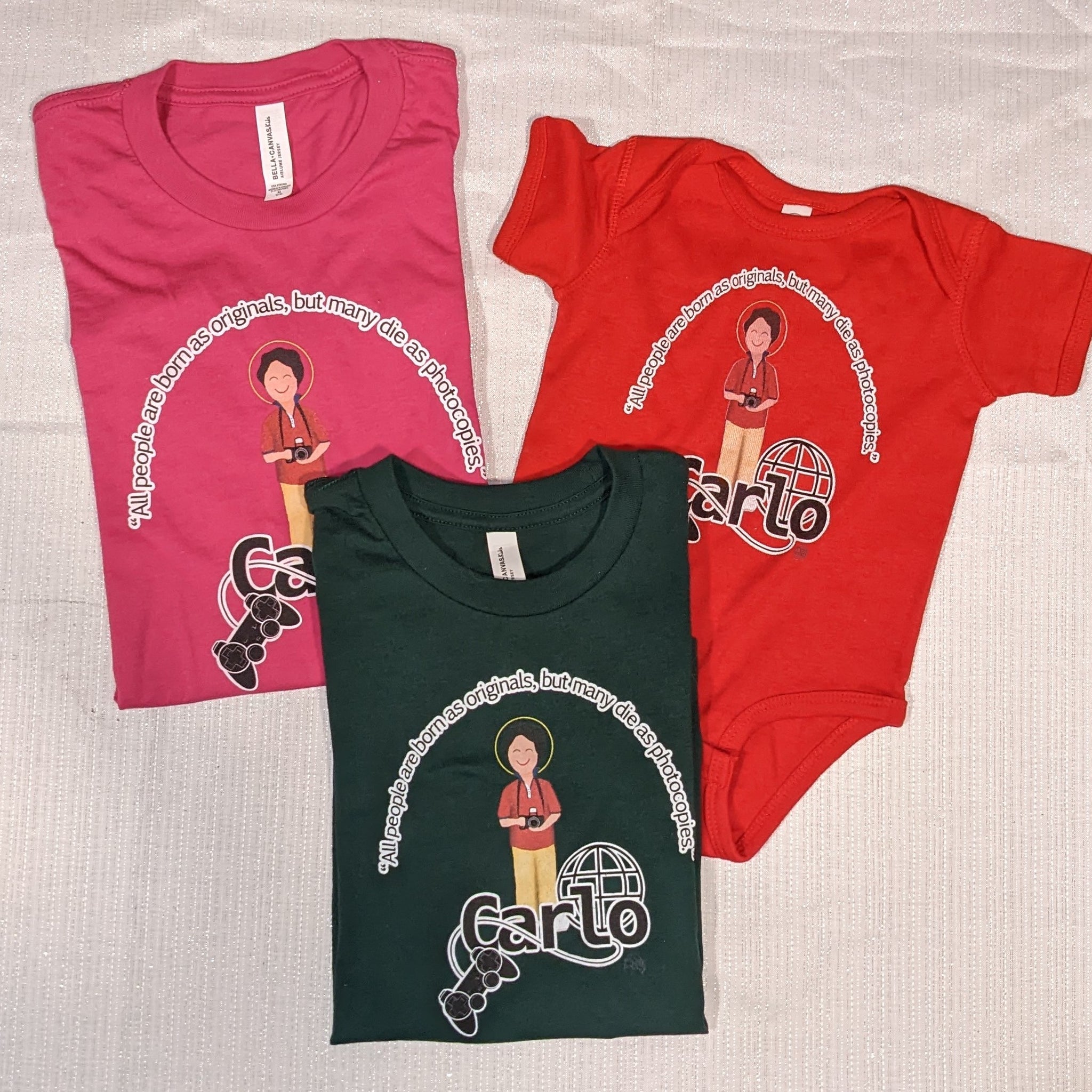 Bl. Carlo Acutis shirts in pink, black, and red - one adult shirt, one toddler shirt, and one baby bodysuit