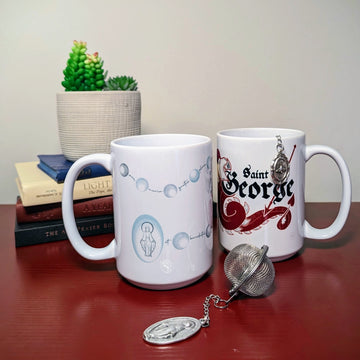 Two Catholic mugs and tea infusers on a table with books. The mugs feature the rosary on one and St. George on the other