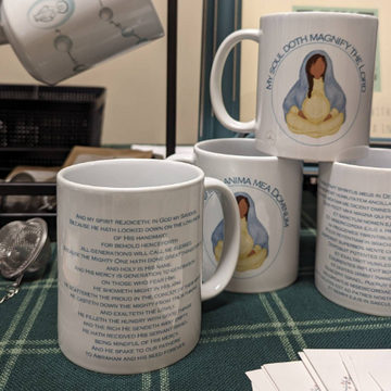 A set of Marian mugs on display. The mugs feature the words of the Magnificat in Latin on the back and an illustration of Mary pregnant with Jesus that says "My Soul Doth Magnify the Lord"
