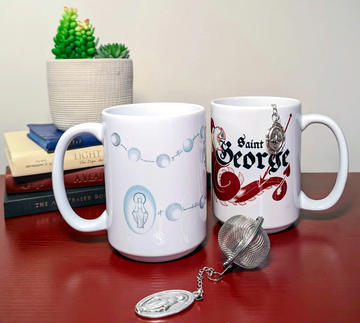 Two Catholic mugs. One mug has a rosary and miraculous medal design while the other mug has a dragon and the name "Saint George" on it. A miraculous medal tea infuser is displayed in front of the two mugs. A Holy Spirit medal is displayed off the side of the St. George mug.
