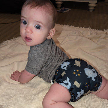 Baby wearing a Catholic cloth diaper. The diaper has whales and scrolls on it to depict the tale of Jonah and the whale.