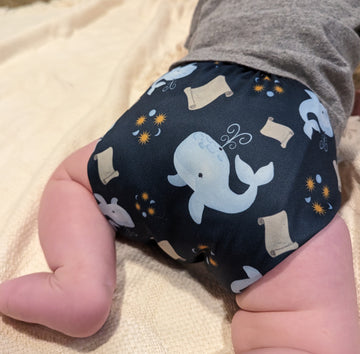 Back of a baby crawling to show a reusable Catholic cloth diaper. The diaper has whales and scrolls on it to depict the tale of Jonah and the whale.