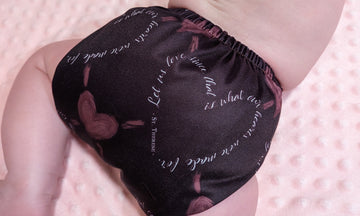 A maroon baby cloth Catholic diaper with hearts on it and the St. Therese of Lisieux quote "Let us love since that is what our hearts were made for." 