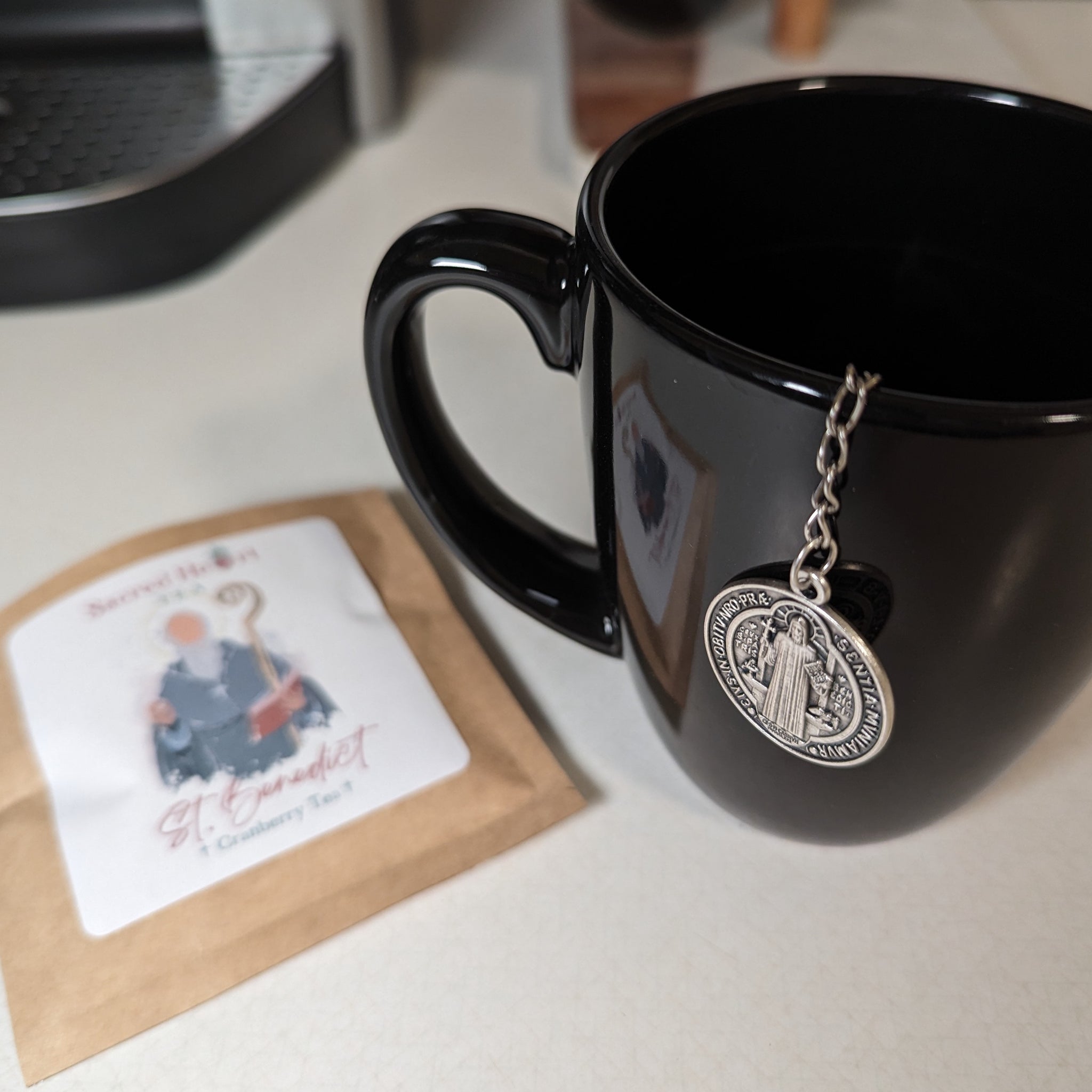 Mug with a Catholic St. Benedict medal tea infuser shown off the side of the mug.