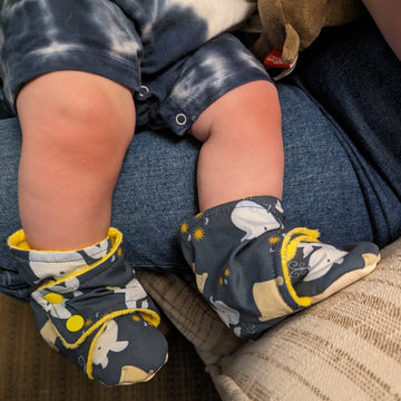 Baby feet wearing Catholic booties. The booties have whales and scrolls on them to represent the story of Jonah and the whale.