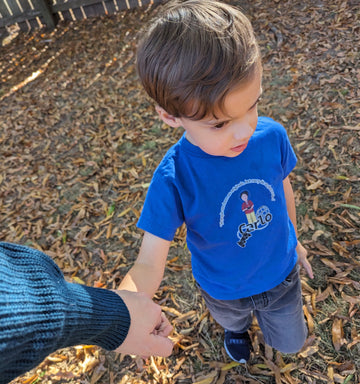 Kid wearing a blue shirt featuring Bl. Carlo Acutis and the quote "All people are born as originals, but many people die as photocopies."