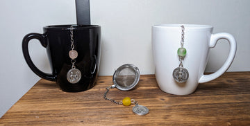 Two mugs displaying three Catholic tea infusers. One is a miraculous medal tea infuser and the other two are Communion of Saints tea infusers.